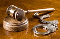 A gavel and block on a richly colored cherry wooden desk with handcuffs.